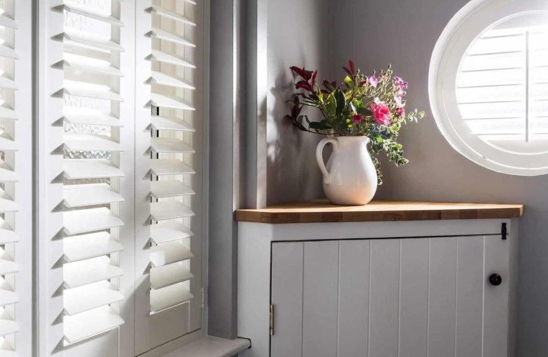 Window shutters beside a dresser and flowers